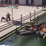 Due gondole ormeggiate ai gradini mentre i gondolieri riposano sotto un ombrellone a Venezia